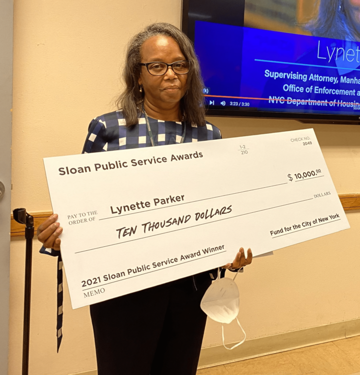 Lynette Parker holds a giant check at her Sloan Public Service Award ceremony